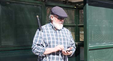 A blind man waiting at a bus stop listens to NFB-NEWSLINE on his mobile phone.